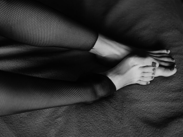 A black and white photograph featuring legs in fishnet stockings on a textured surface.